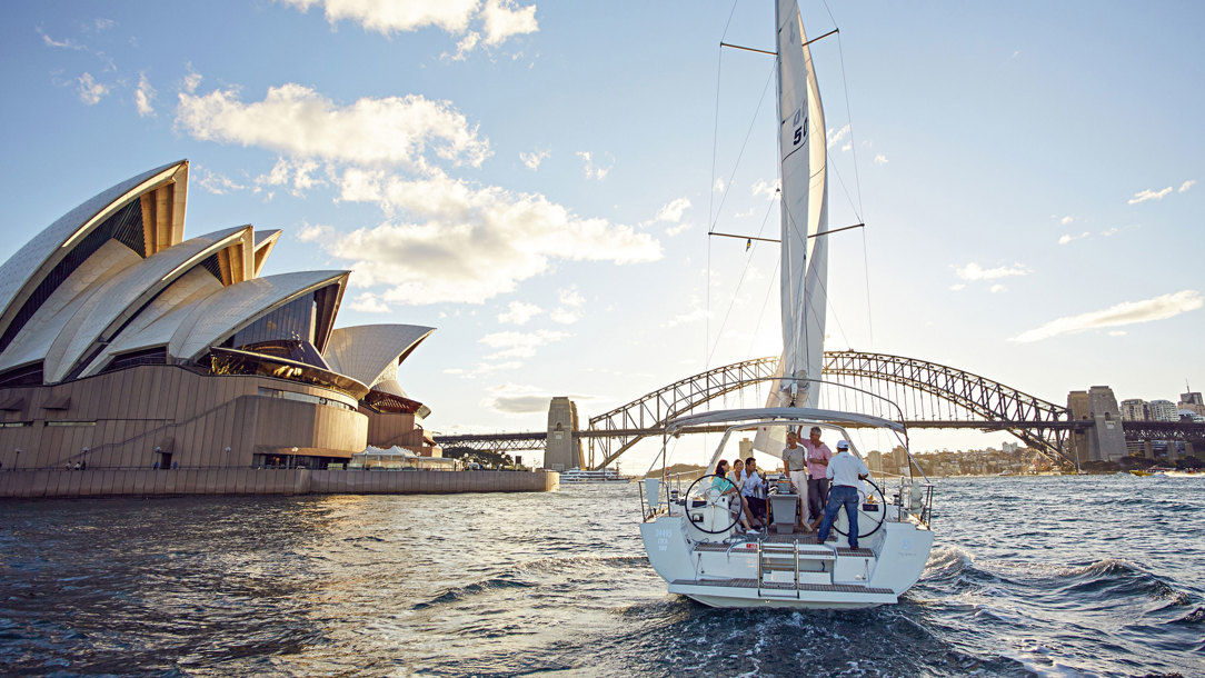 A group of people sailing on a yacht through Sydney Harbour, passing the Opera House.