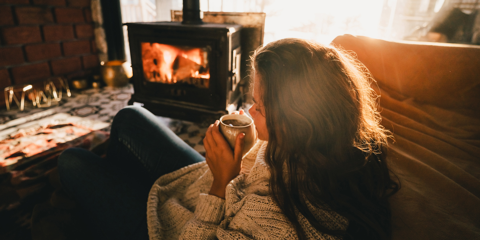 A woman having a hot drink next to a fire.